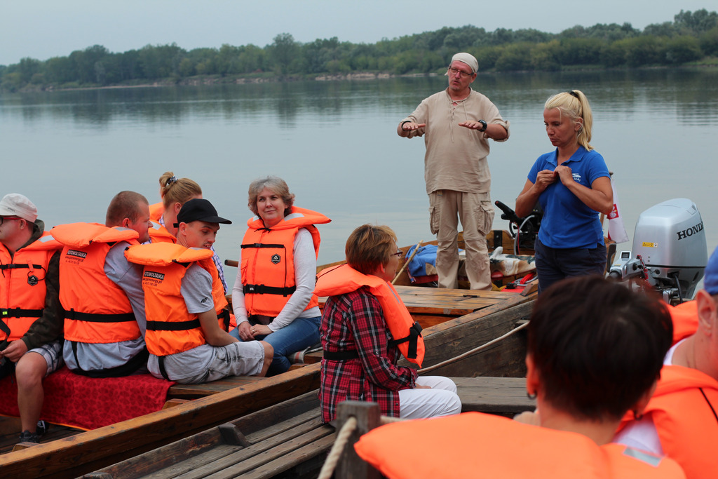 Grupa osób w kamizelkach ratunkowych czeka na odpłynięcie łodzi